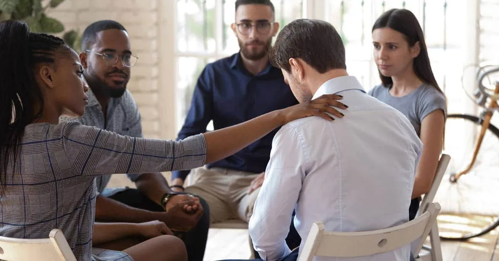 Group therapy member comforting a man with a hand on his shoulder, illustrating what addiction therapy programs are