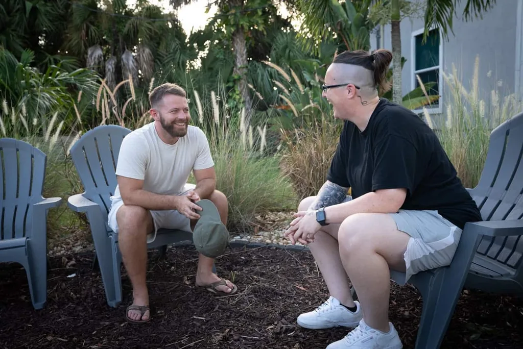 Two men talking face to face in Adirondack chairs in the facility garden, illustrating what addiction treatment involves