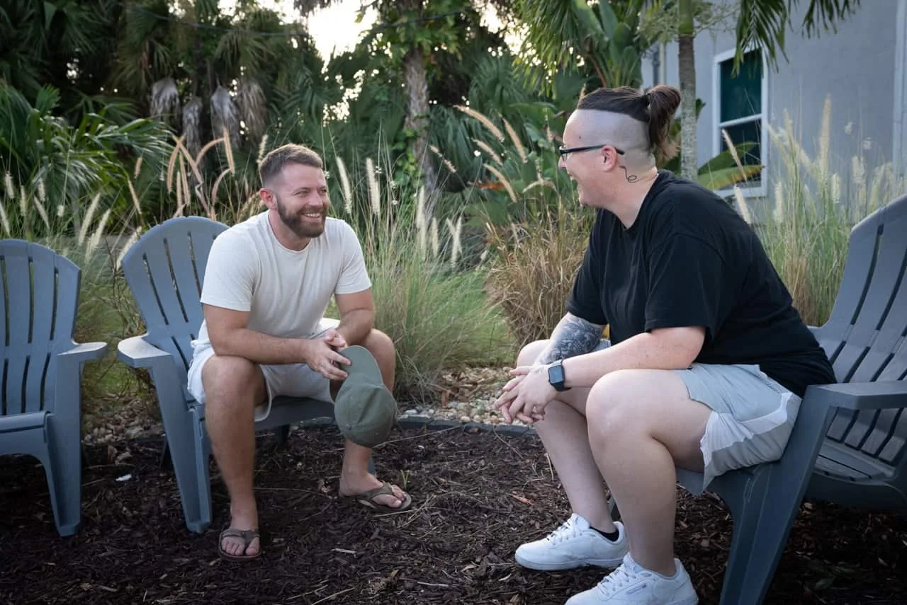 Two men talking face to face in Adirondack chairs in the facility garden, illustrating what addiction treatment involves