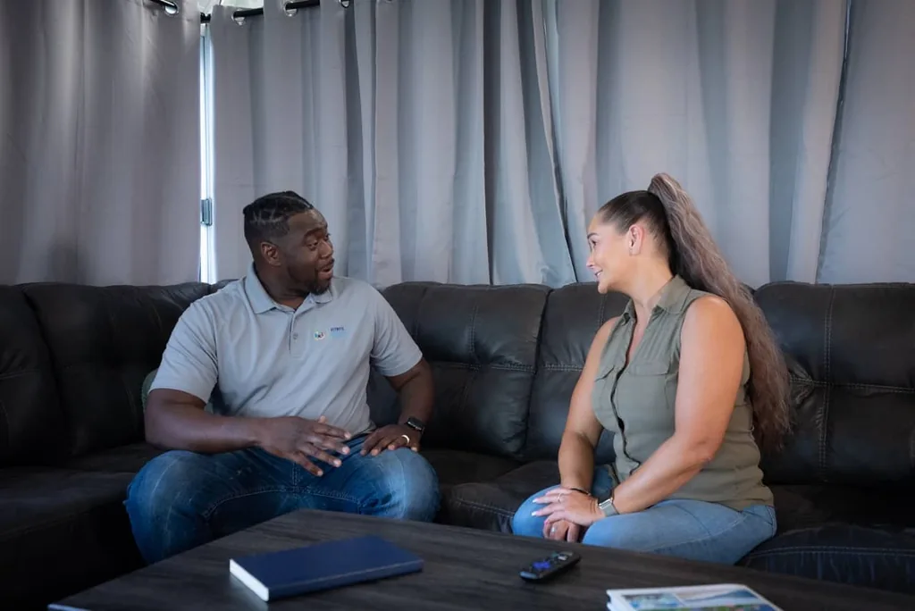 Man and woman talking on a dark leather sofa in a softly lit room, illustrating a counseling session in addiction treatment