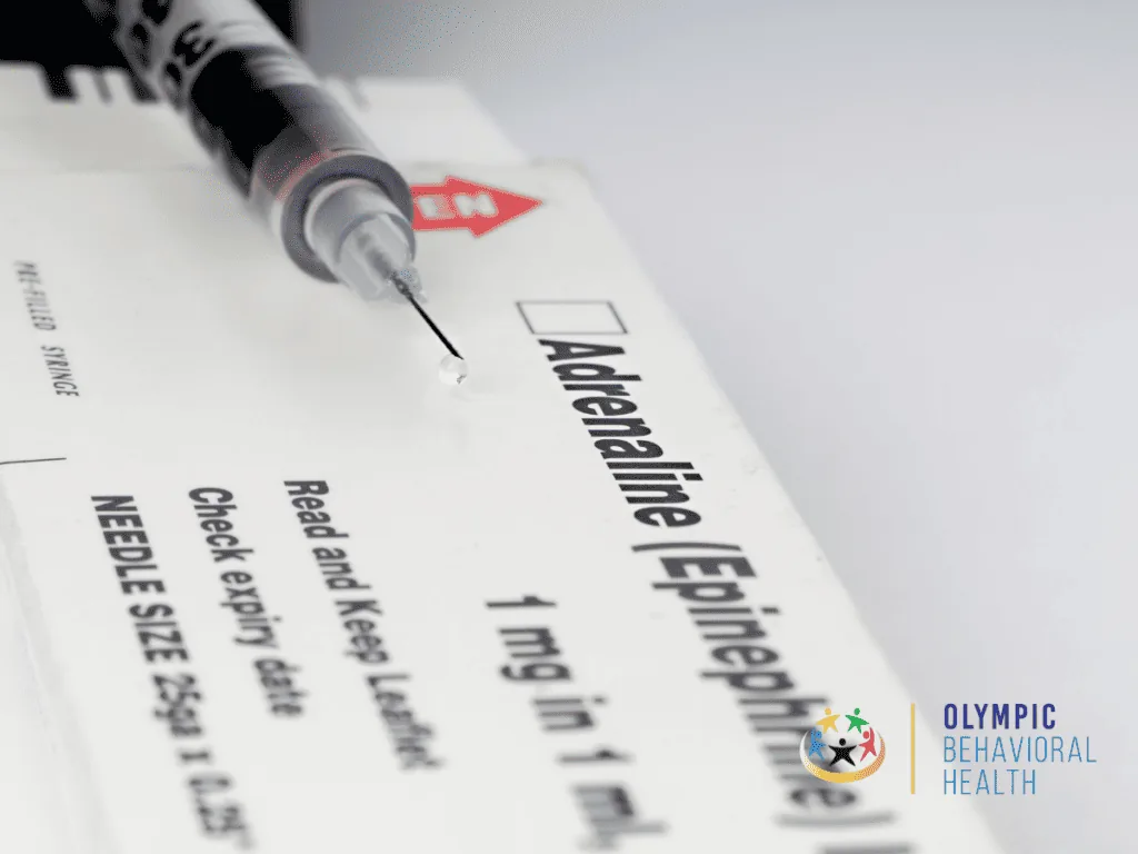 Syringe resting on a box labeled Adrenaline (Epinephrine) 1 mg in 1 ml, accompanying the definition of addiction