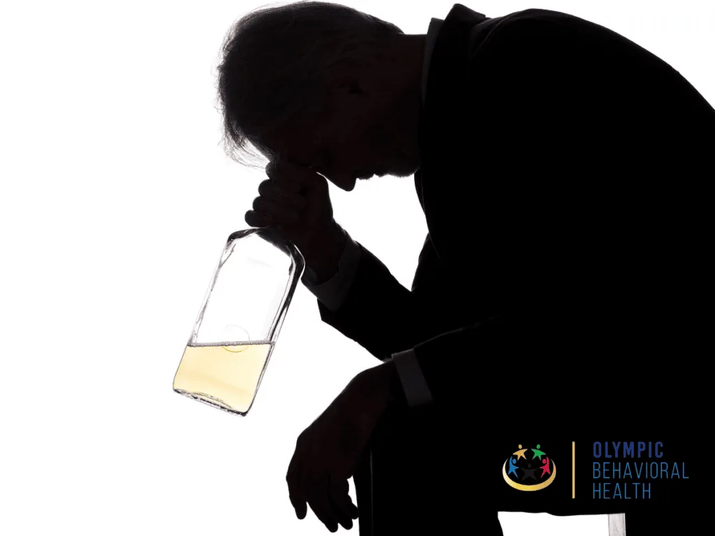 Silhouette of a man hunched over with his head in his hand, holding a liquor bottle, showing alcohol-related disease