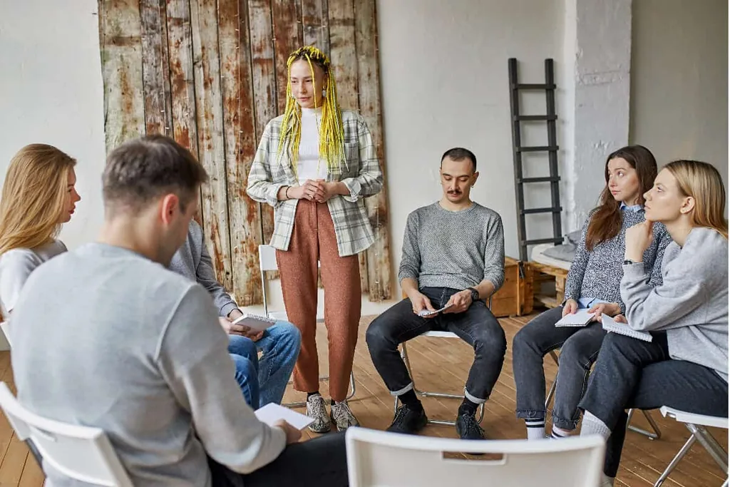 Peer support group in a circle listening to a woman speak, illustrating motivation and commitment in Alcoholics Anonymous
