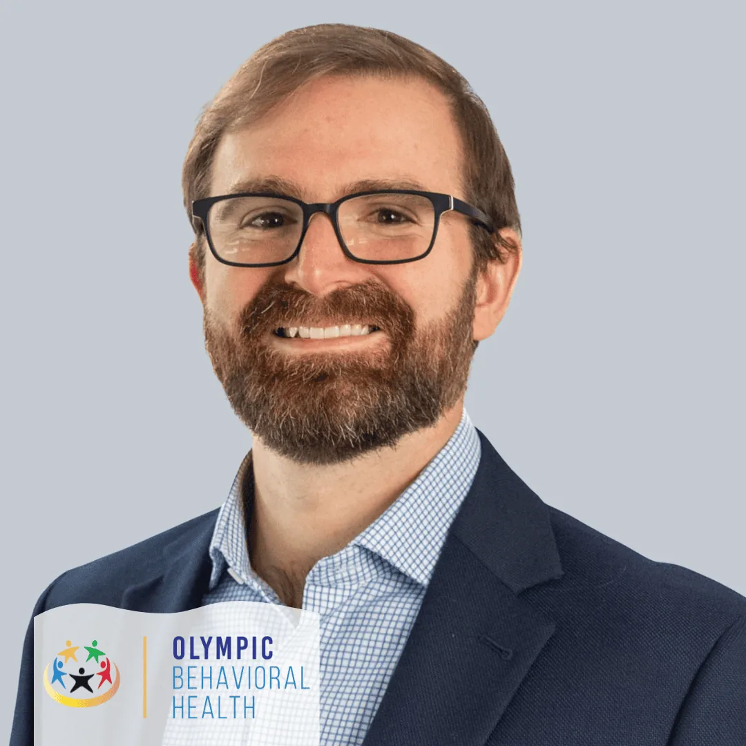Andrew Spahn, Co-Founder and CEO of Olympic Behavioral Health, smiling in glasses and a navy blazer