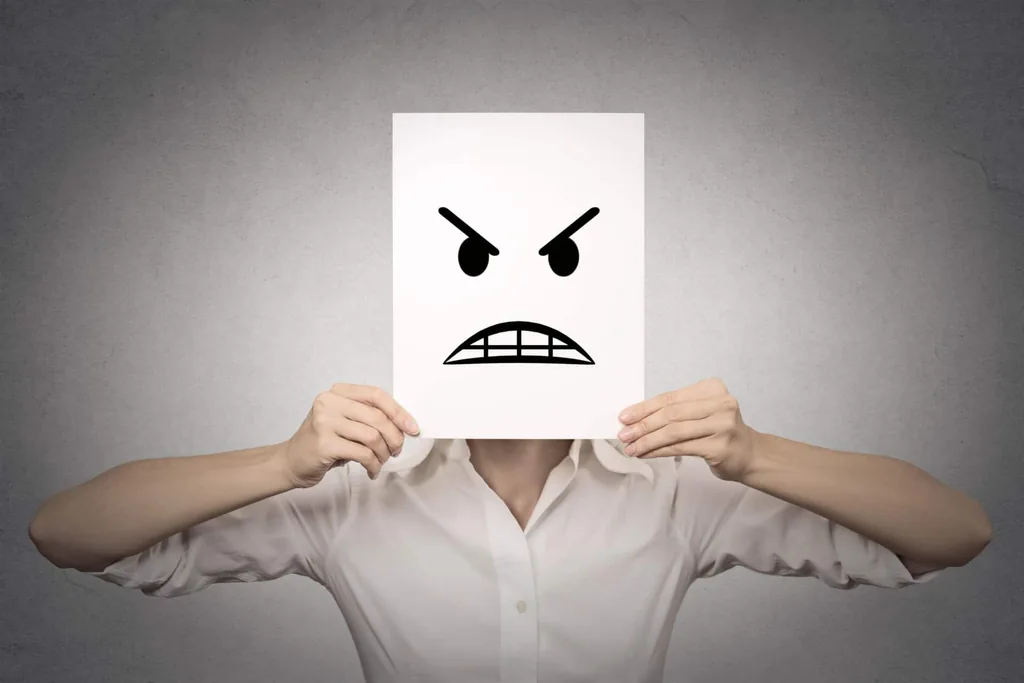 Person hiding their face behind a paper with an angry drawn face, introducing anger management in recovery