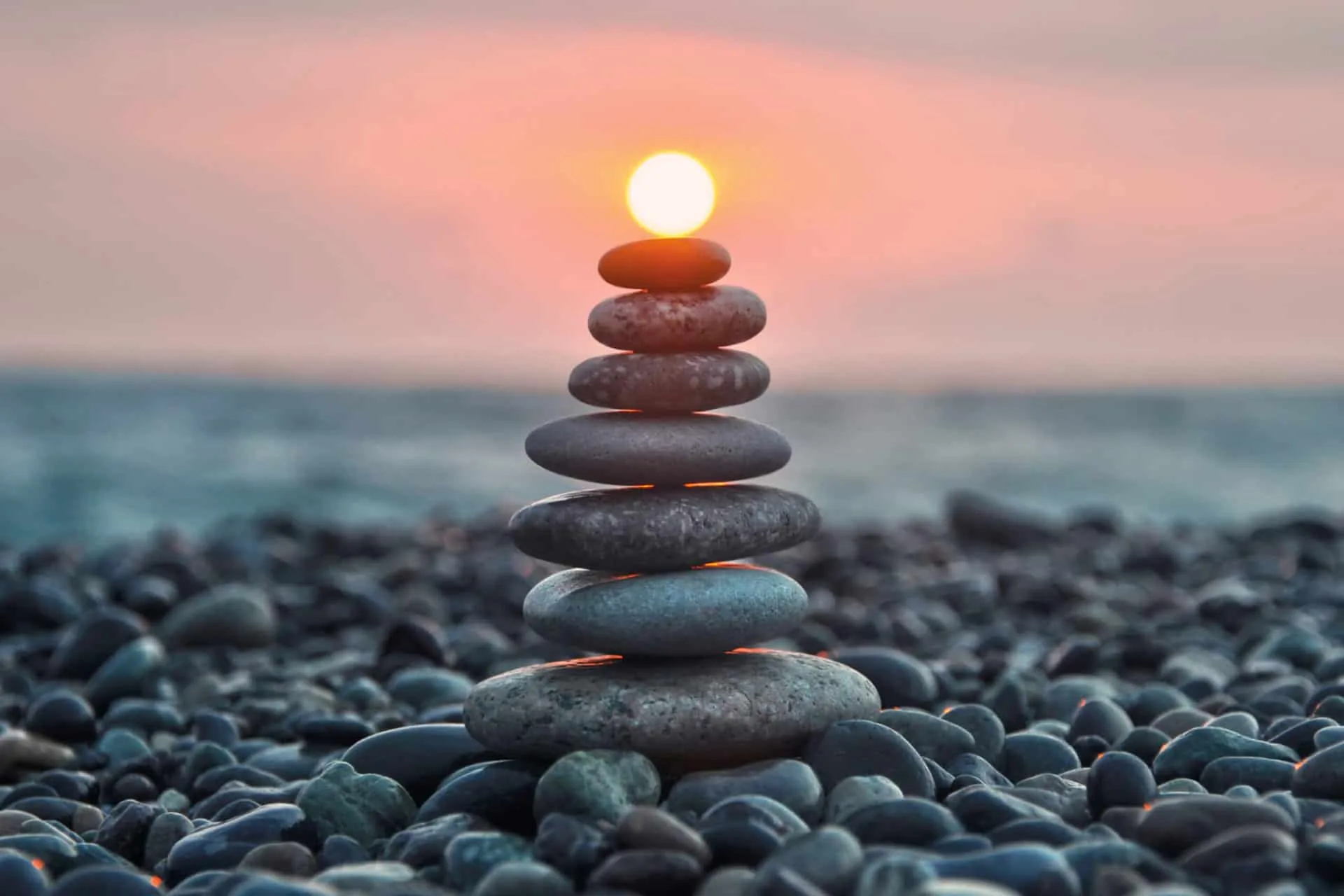 Stack of smooth balanced stones on a pebble beach with the sun at the top, used as the staff page header image