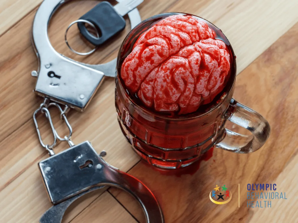 Brain-shaped red gelatin in a beer mug beside handcuffs and car keys, showing how drugs hijack natural reward