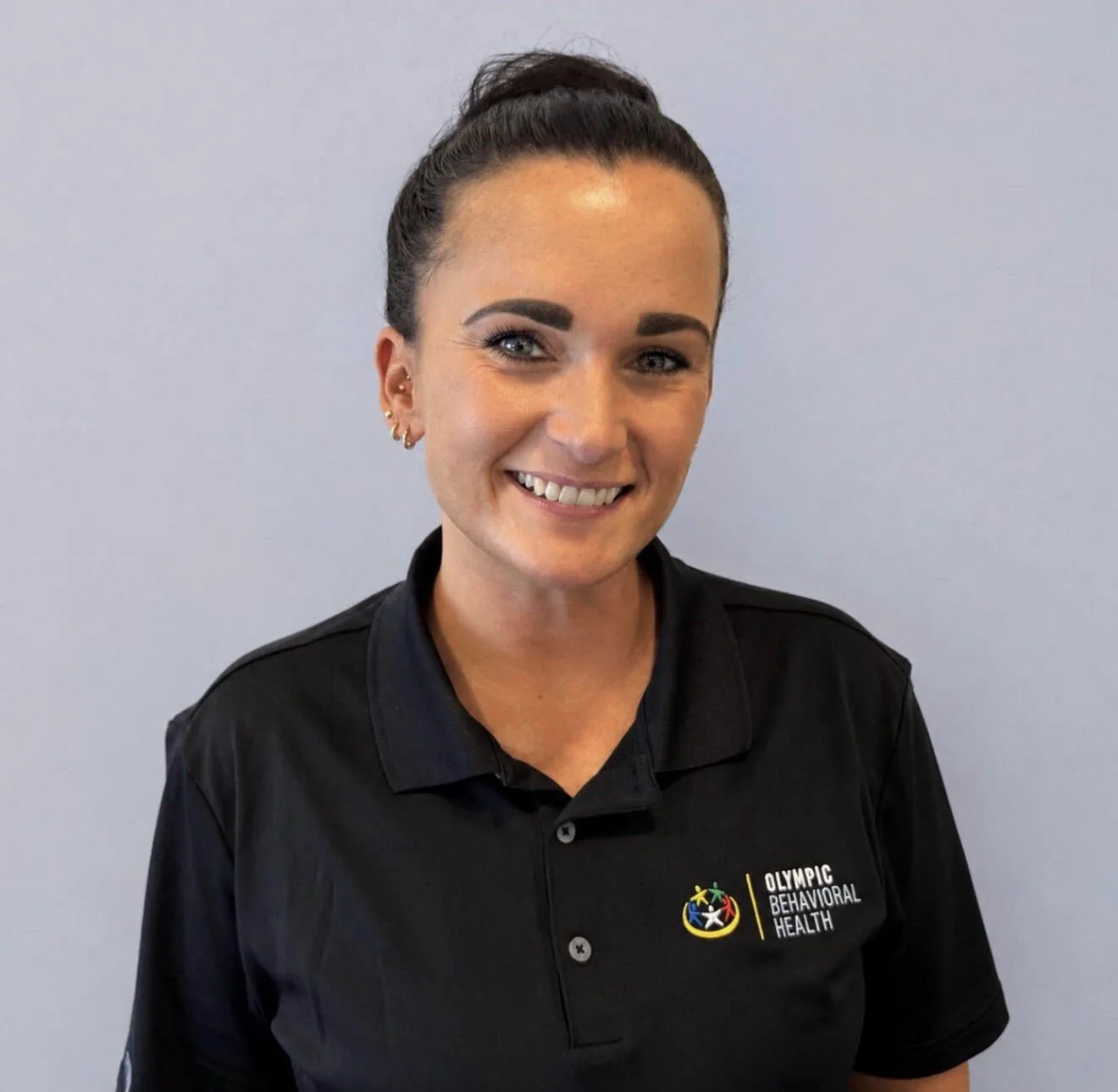 Cassie Reimel, Lead Behavioral Health Technician at Olympic Behavioral Health, smiling in a branded black polo shirt