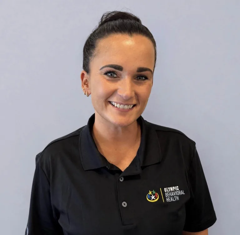 Cassie Reimel, Lead Behavioral Health Technician at Olympic Behavioral Health, smiling in a branded black polo shirt