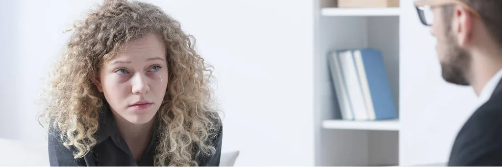 Worried woman with curly hair speaking with a therapist, illustrating what complex PTSD is