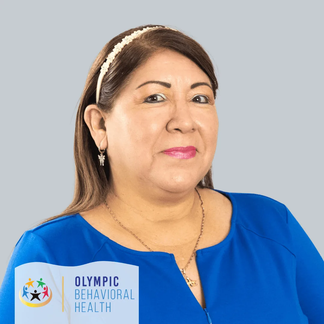 Cynthia Flores, Administrative Assistant at Olympic Behavioral Health, smiling in a blue top against a gray backdrop
