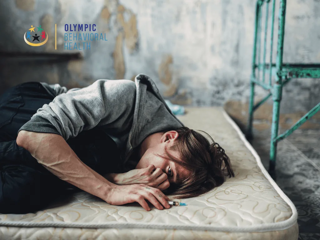 Young man curled up on a bare mattress beside a syringe in a run-down room, showing the toll of drug addiction
