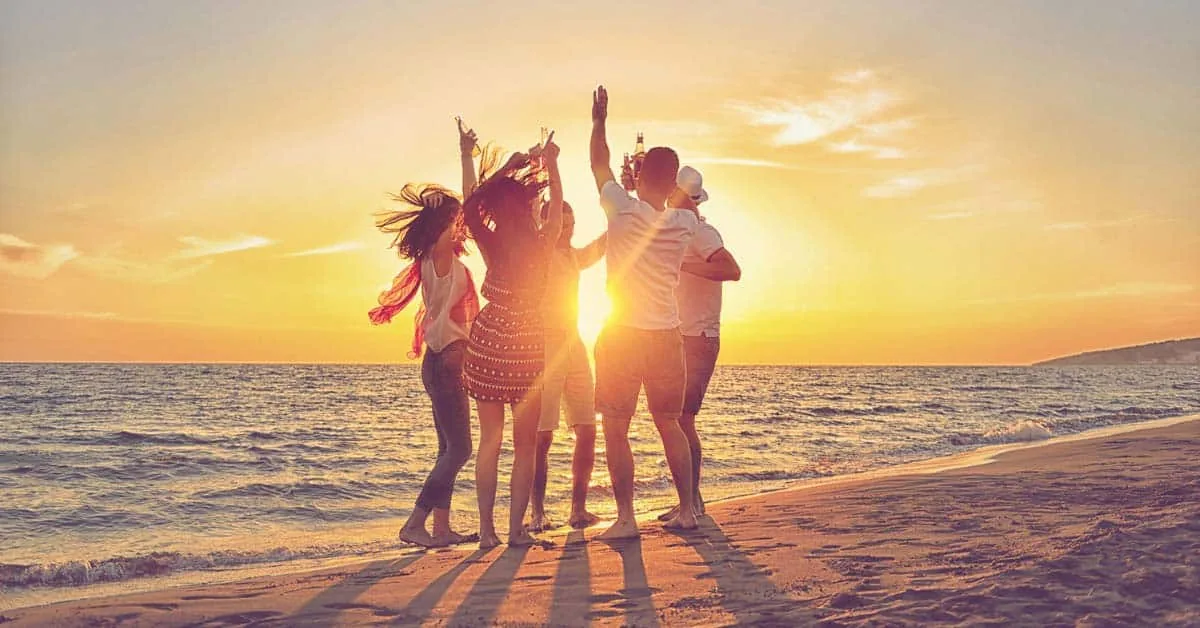 Group of friends dancing on a beach at sunset, illustrating a fulfilling sober life after drug addiction treatment