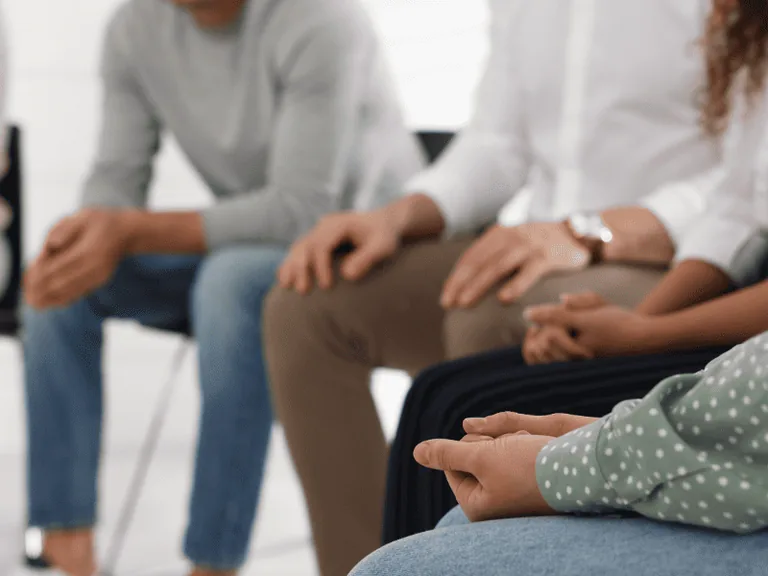 Close-up of people seated in a circle during a group therapy session for drug, alcohol and mental health treatment