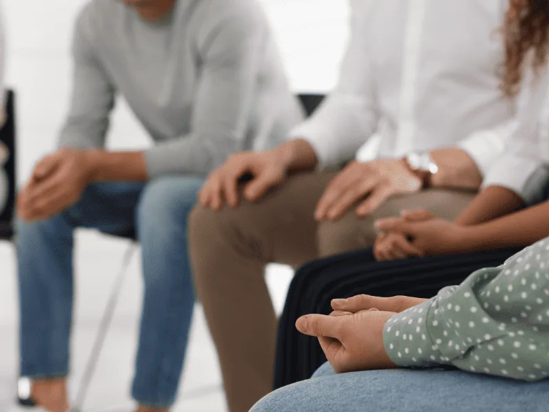 Close-up of people seated in a circle during a group therapy session for drug, alcohol and mental health treatment