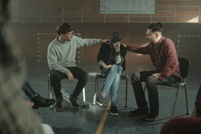 Group therapy circle where two men comfort a distressed participant, illustrating psychotherapy and counselling for addiction