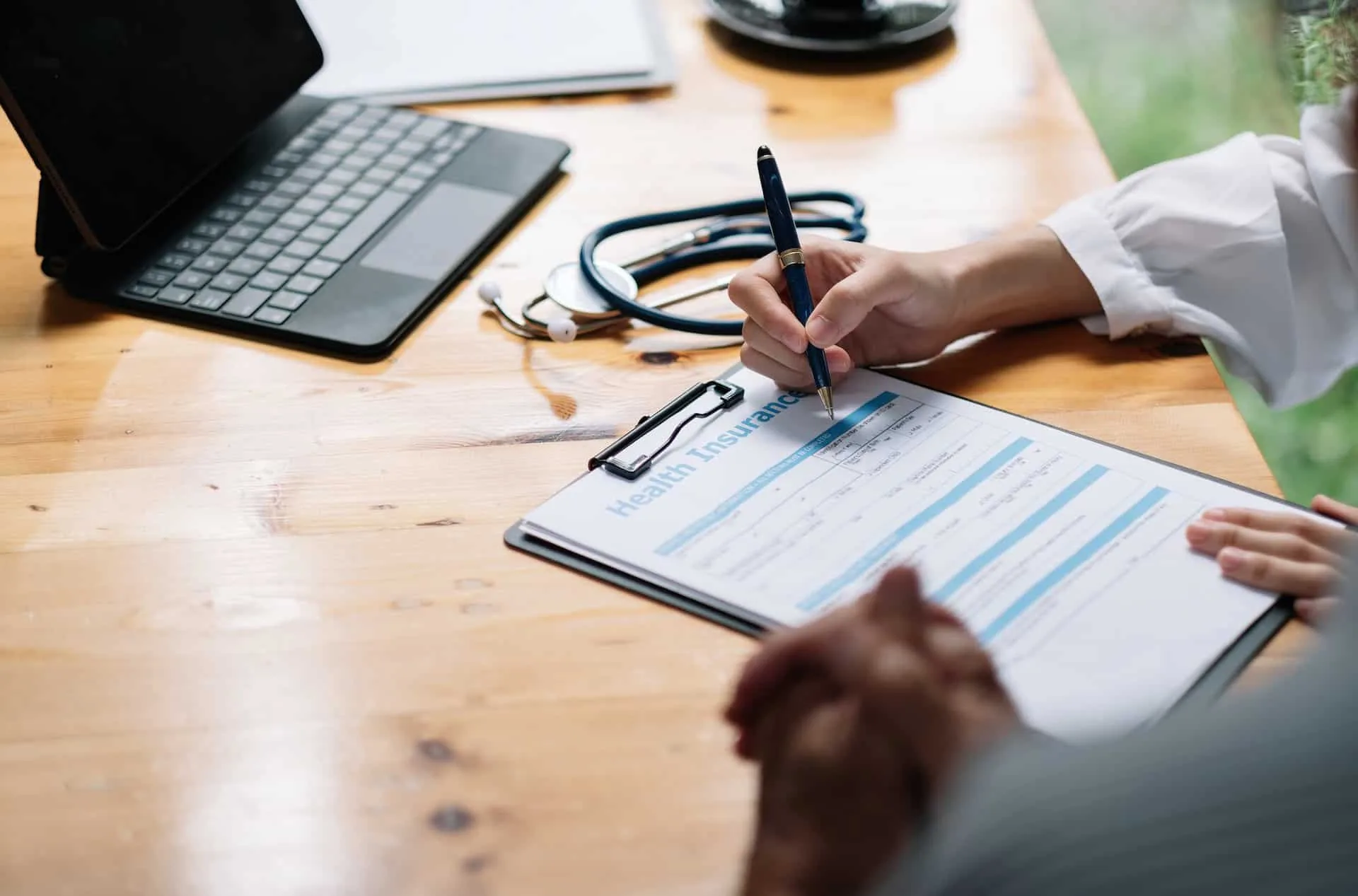 Patient filling out a health insurance form on a clipboard at a desk with a stethoscope, beside Greenacres addiction info