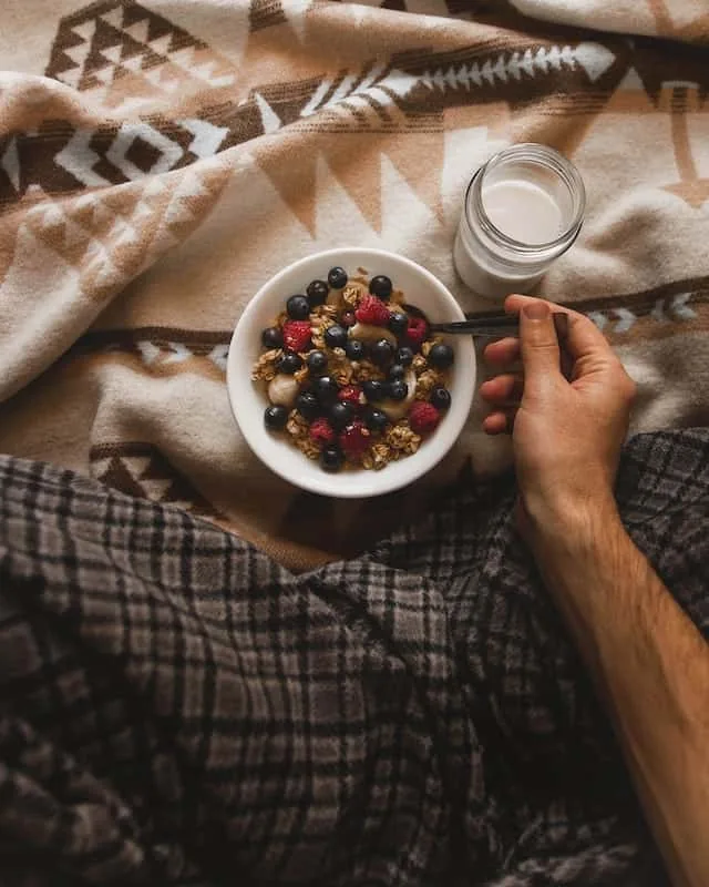 Hands holding a bowl of granola and berries over a patterned blanket, showing nourishing food in holistic therapy