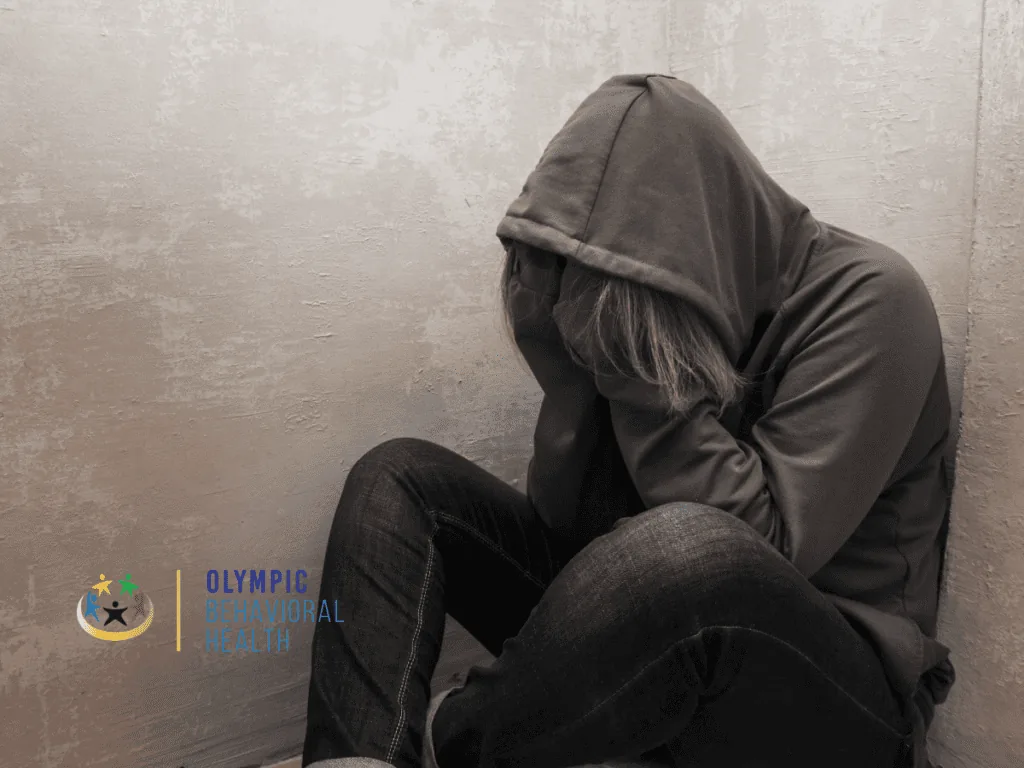 Person in a gray hoodie sitting on the floor against a wall with head down, depicting the distress linked to hyponatremia