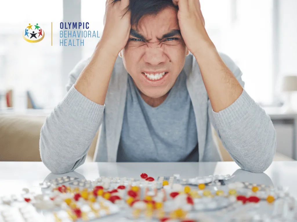 Stressed man gripping his head over a table covered in pills, illustrating drug use as a cause of hyponatremia