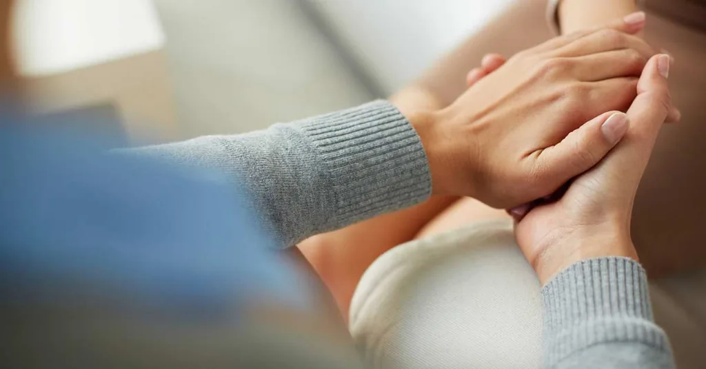 Therapist gently holding a client's clasped hands in a gesture of comfort during individual therapy