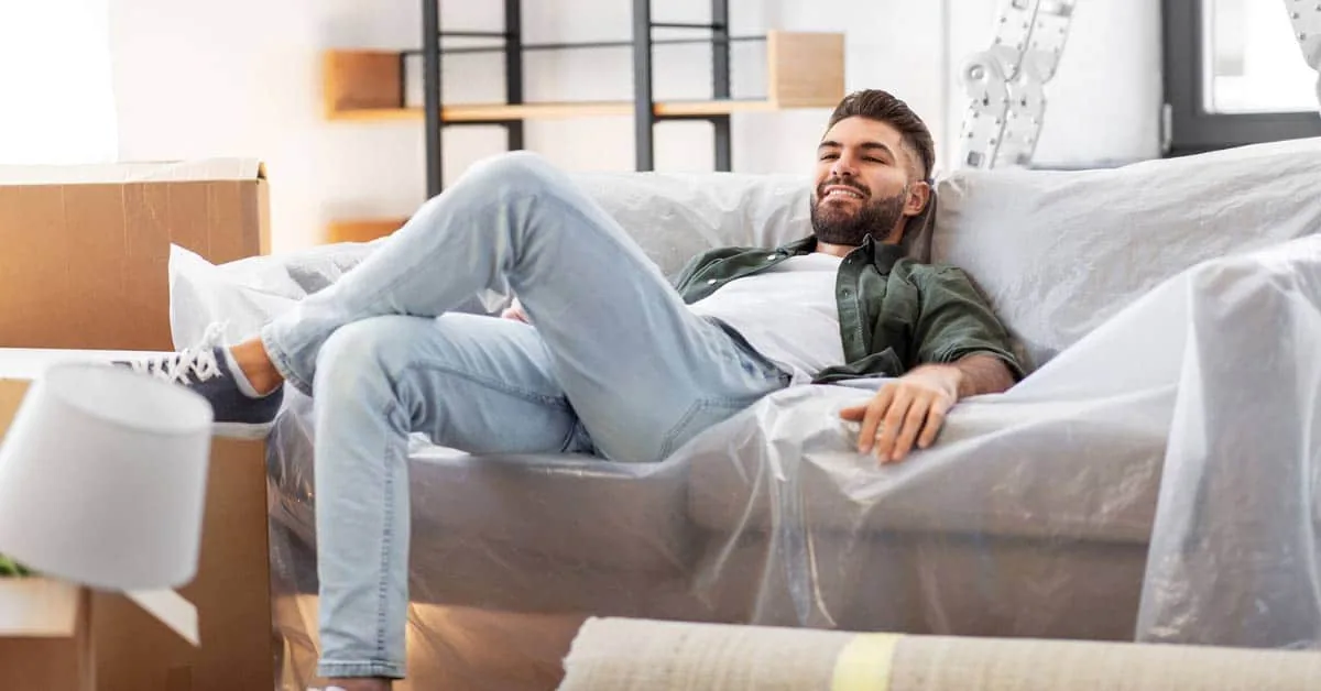 Smiling man relaxing on a sheet-covered sofa among moving boxes, illustrating a fresh start with individual therapy