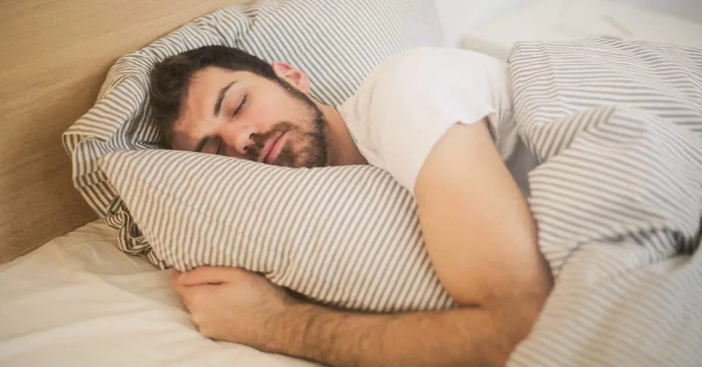Man sleeping peacefully in bed under striped bedding, illustrating the restful brain states neurofeedback therapy targets