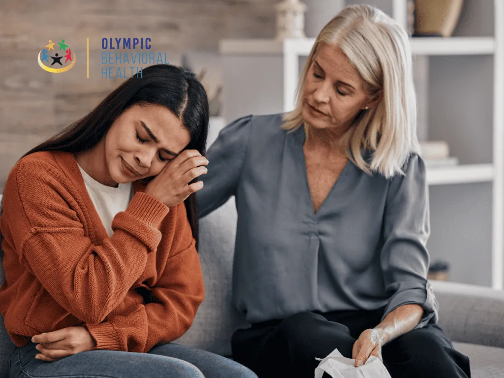 Older woman comforting a tearful young woman on a couch, showing family support for mental health and addiction