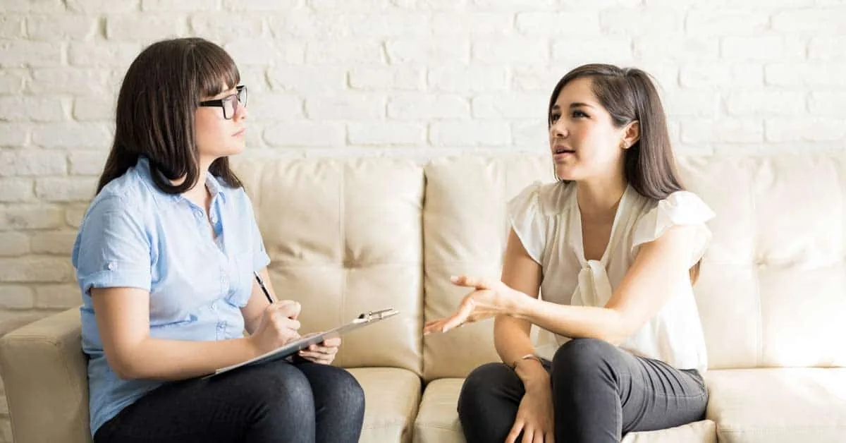 Therapist with a clipboard listening to a woman speaking on a sofa during a motivational interviewing session