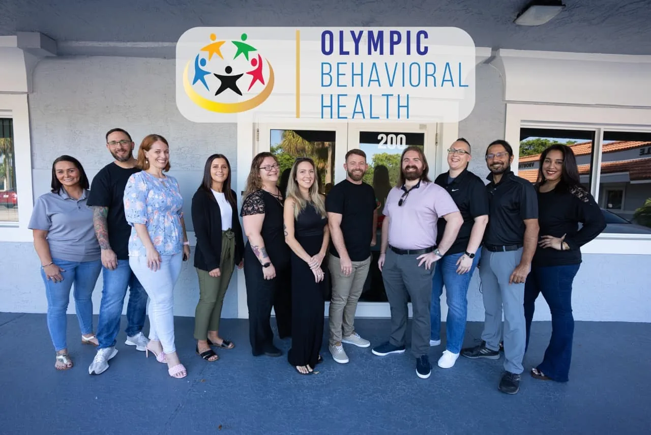 Olympic Behavioral Health staff posing outside the Suite 200 entrance beneath the Olympic Behavioral Health logo sign