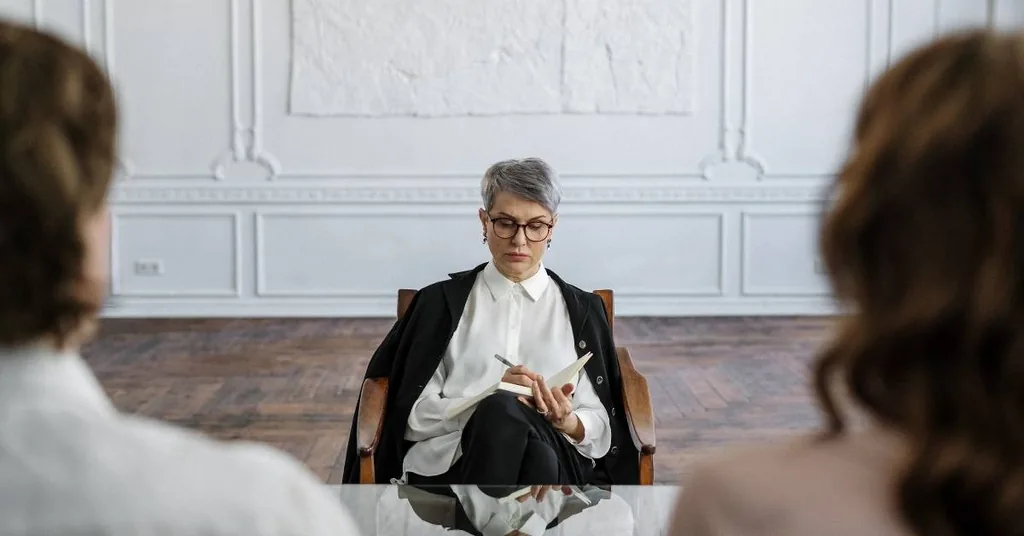 Therapist with glasses taking notes while facing two clients, introducing the article on opioid withdrawal symptoms