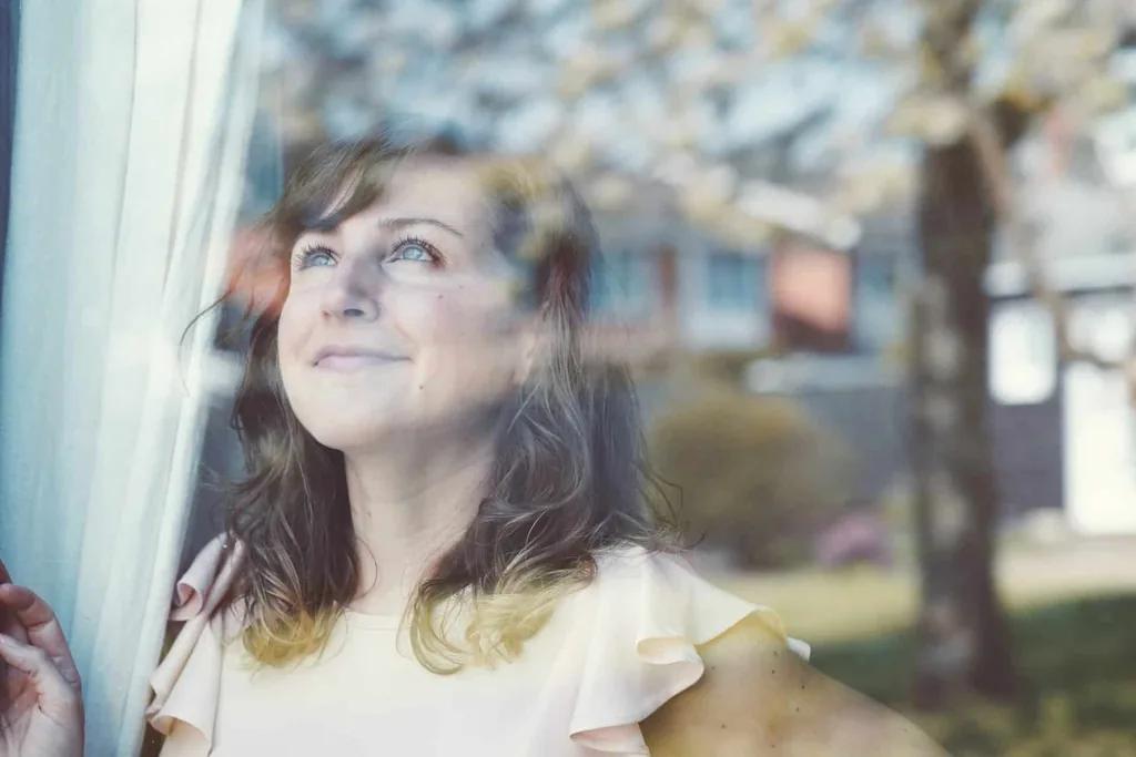 Hopeful woman gazing out a sunny window, illustrating person-centered language to overcome addiction stigma