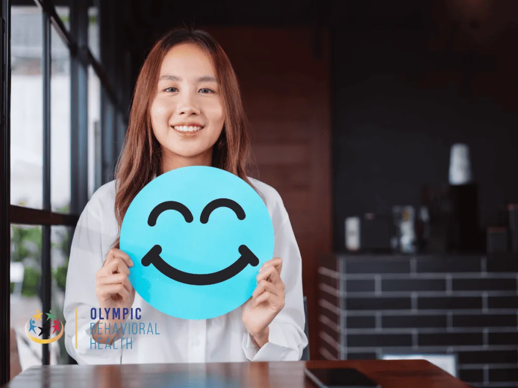 Smiling young woman holding a blue smiley face sign, illustrating the mood-related functions of oxytocin