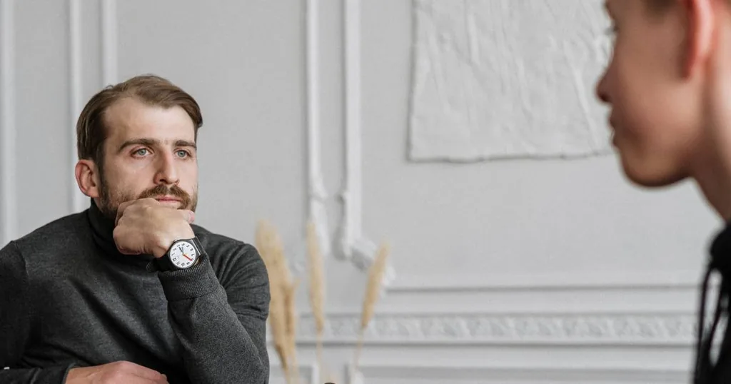 Thoughtful man resting his chin on his hand while listening to a therapist during psychotherapy for addiction