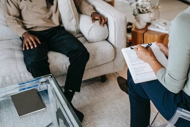 Counselor with a clipboard of notes sitting across from a client on a sofa during a psychotherapy session
