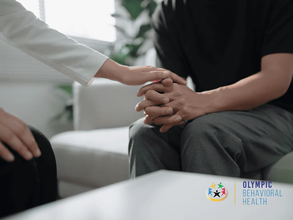 Clinician gently resting a hand on a patient's clasped hands, showing support for co-occurring PTSD and addiction