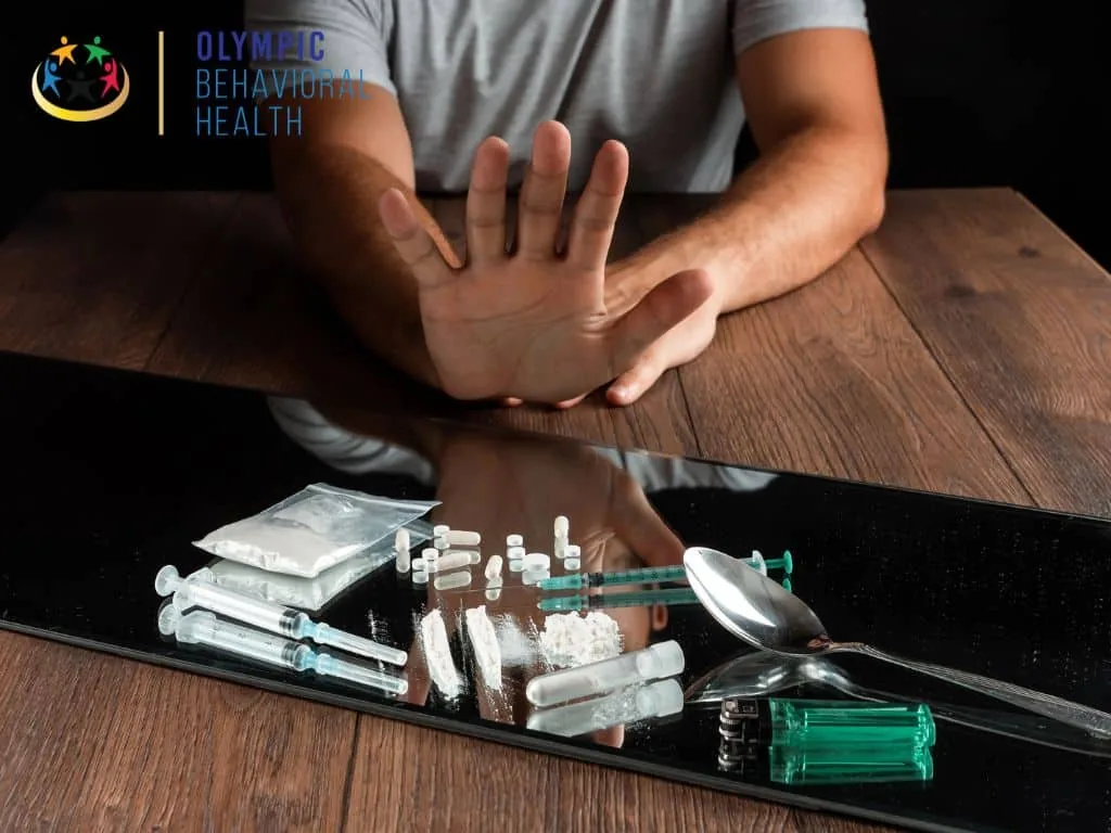 Person holding up a hand to refuse drugs, pills and syringes on a table, illustrating dangers of hallucinogen addiction