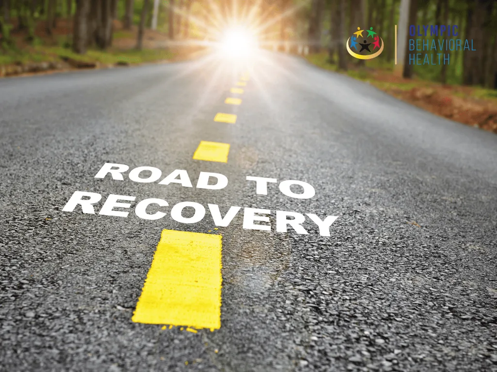 Words ROAD TO RECOVERY painted on a sunlit asphalt road through a forest, illustrating encouraging words about recovery