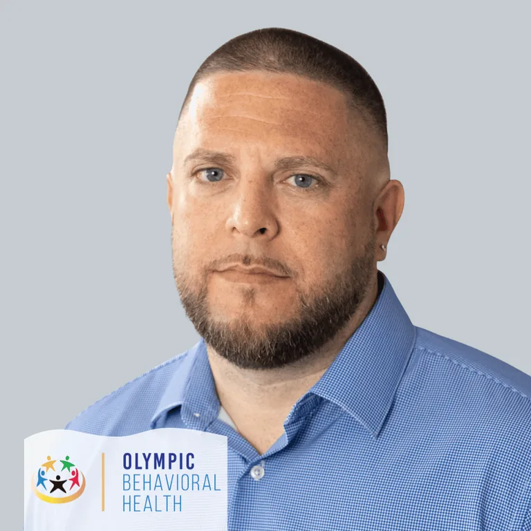 Ryan Yonkers, Alumni Coordinator at Olympic Behavioral Health, in a blue button-down shirt against a gray backdrop
