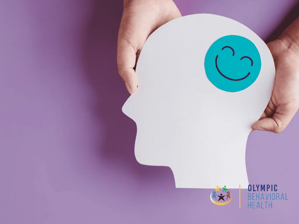 Hands holding a paper head cutout with a teal smiling face on a purple background, symbolizing serotonin and mood