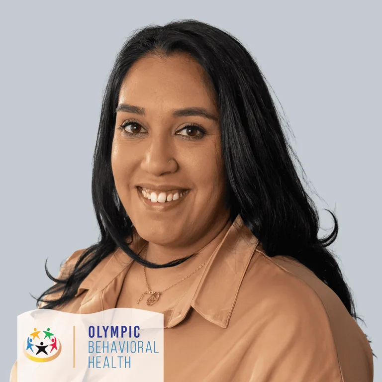 Stephanie Susu, Director of Operations at Olympic Behavioral Health, smiling in a tan blouse against a gray backdrop