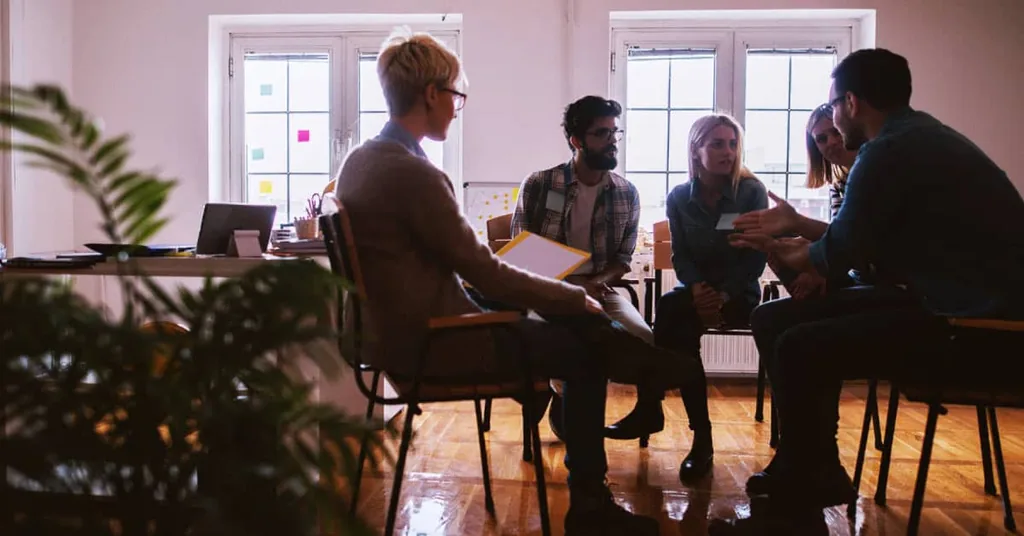 Group therapy circle seated in a sunlit room, illustrating what group therapy is and how peer support helps