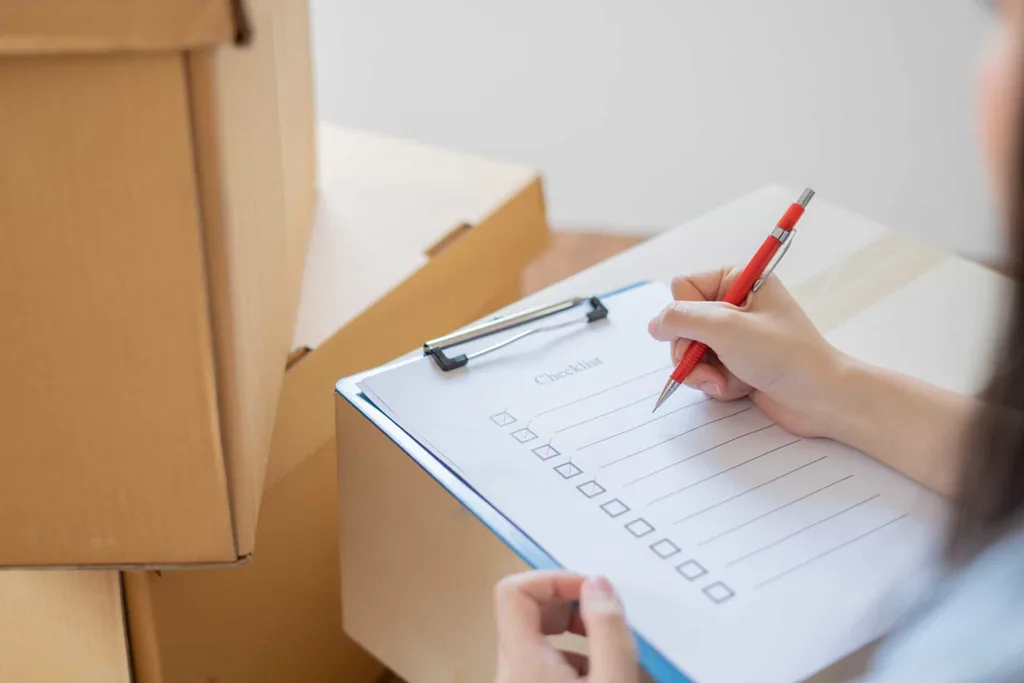 Person checking off a checklist on a clipboard beside packed boxes, preparing what to bring to rehab