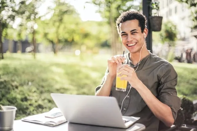 Smiling young man with a drink and laptop at an outdoor table, showing benefits of psychotherapy for addiction